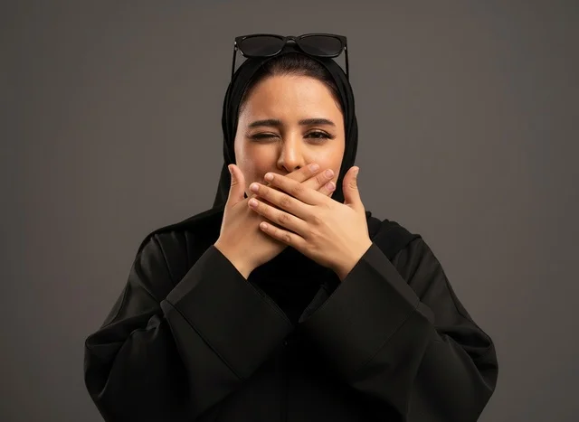 امرأة إماراتية بالعباءة تغمز على خلفية رمادية