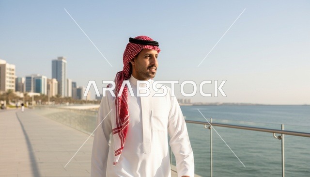 رجل سعودي يسير على الممشى البحري مع خلفية المدينة
