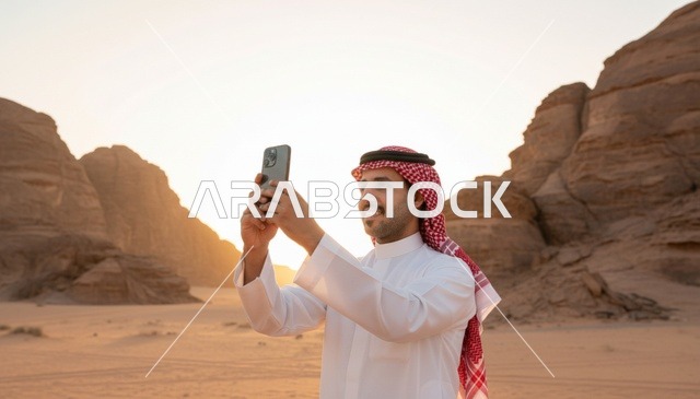 رجل سعودي يستخدم الهاتف الذكي في الصحراء وقت الغروب