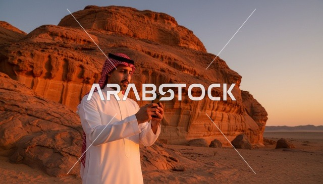 رجل سعودي يستخدم الجوال في الصحراء عند غروب الشمس