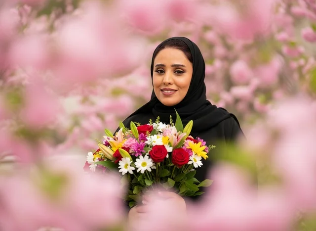 امرأة سعودية بالعباءة تحمل باقة زهور ملونة