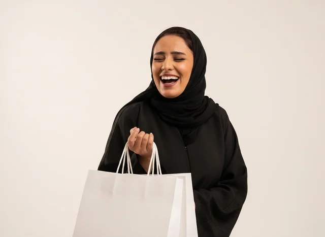 امرأة سعودية سعيدة بالعباءة تحمل أكياس تسوق بيضاء