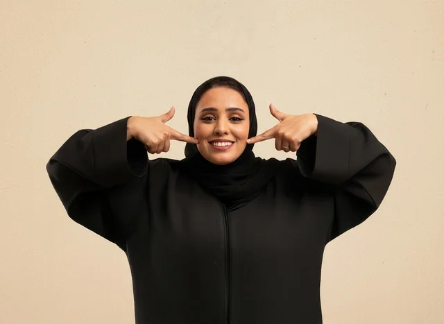 امرأة سعودية سعيدة بالعباءة تشير على ابتسامة