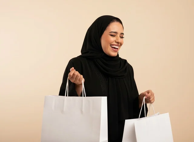 امرأة سعودية مبتسمة تحمل حقائب تسوق بيضاء