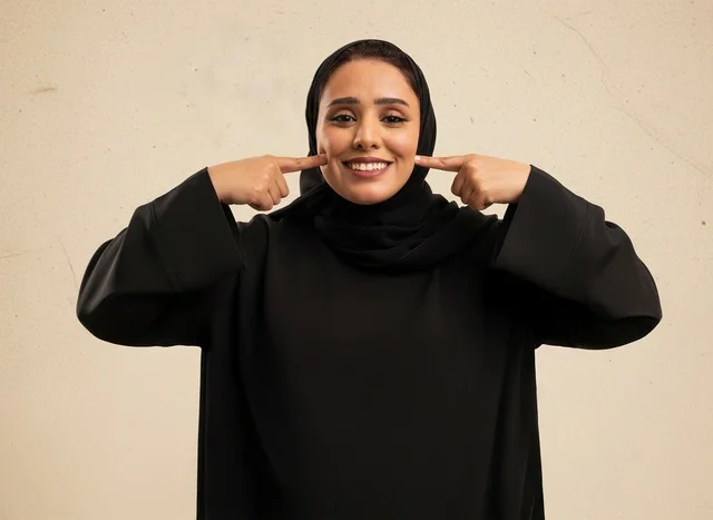 امرأة سعودية سعيدة بالعباءة تشير على ابتسامة