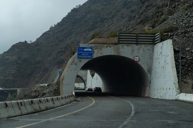 مدخل نفق خرساني على طريق جبلي مع لوحة إرشادية