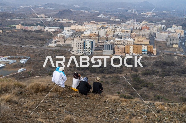 أشخاص يجلسون على تلة تطل على مدينة سعودية جبلية