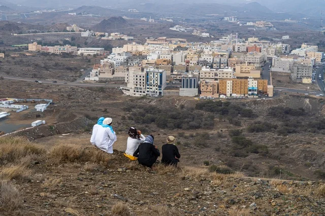أشخاص يجلسون على تلة تطل على مدينة سعودية جبلية