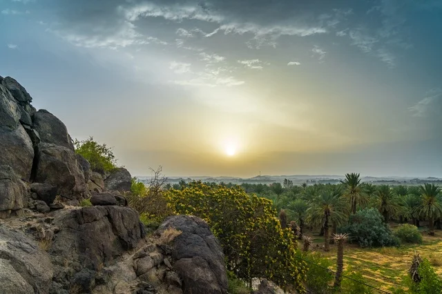 غروب الشمس فوق واحة النخيل والجبال الصحراوية