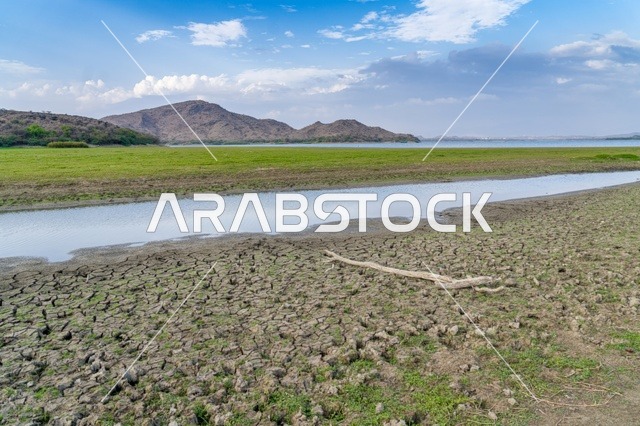 مشهد الأرض الجافة المتشققة مع مساحات خضراء وجبال