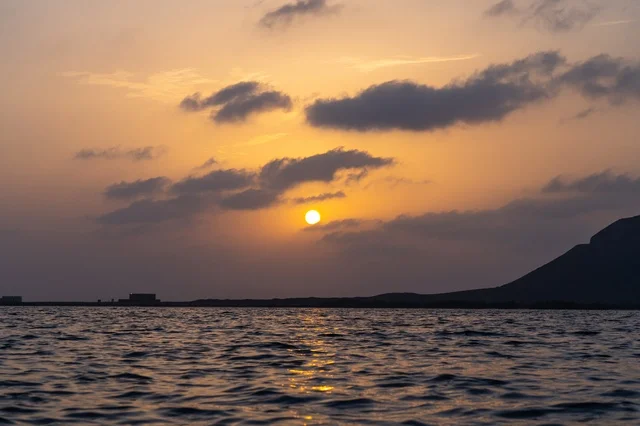 مشهد غروب الشمس فوق مياه البحر مع ظل الجبل والسحب الداكنة