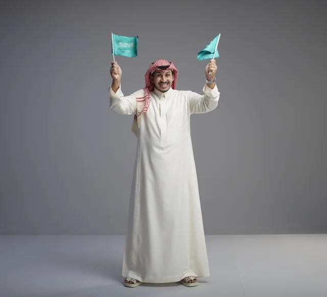 رجل سعودي بالزي التقليدي يحمل العلم الوطني السعودي