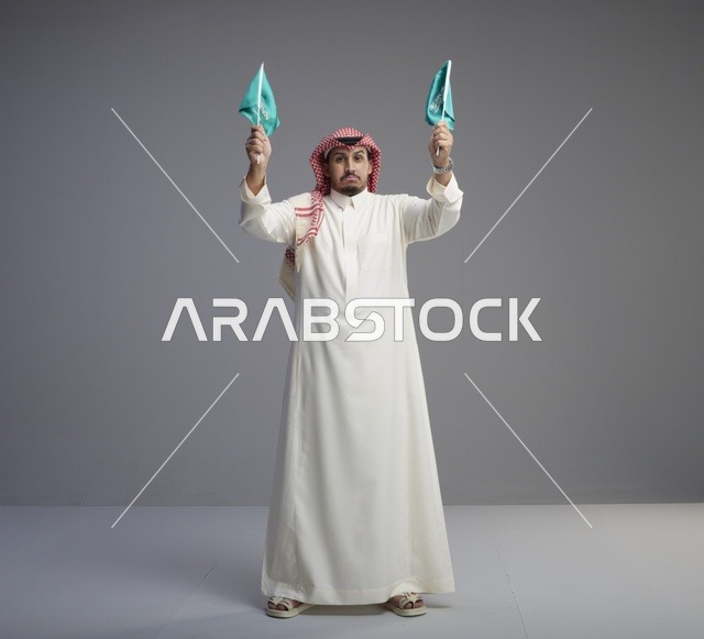 رجل سعودي يرفع العلم السعودي بالزي التقليدي في الاستوديو