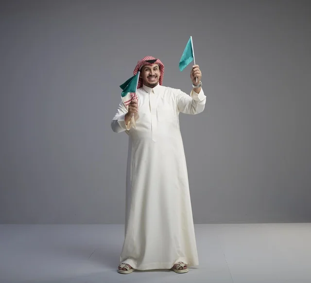 رجل سعودي يحمل أعلام المملكة العربية السعودية بالزي التقليدي