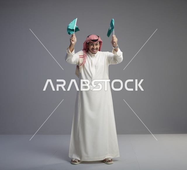 رجل سعودي يحمل علم السعودية بخلفية رمادية