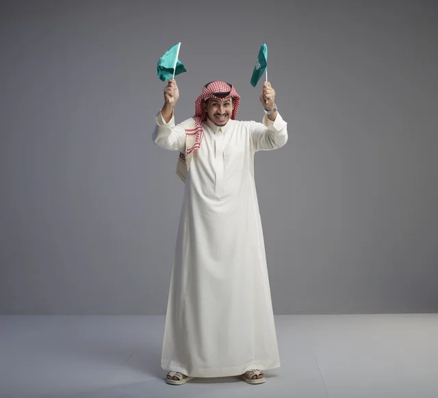 رجل سعودي يحمل علم السعودية بخلفية رمادية
