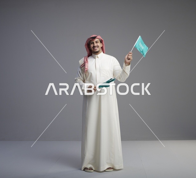 Saudi Man Holding National Flags Against Gray Background - Photo
