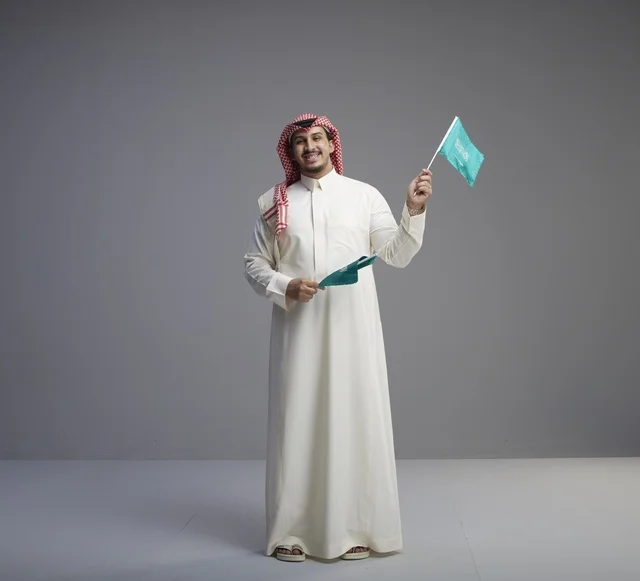 رجل سعودي يحمل الأعلام السعودية بخلفية رمادية