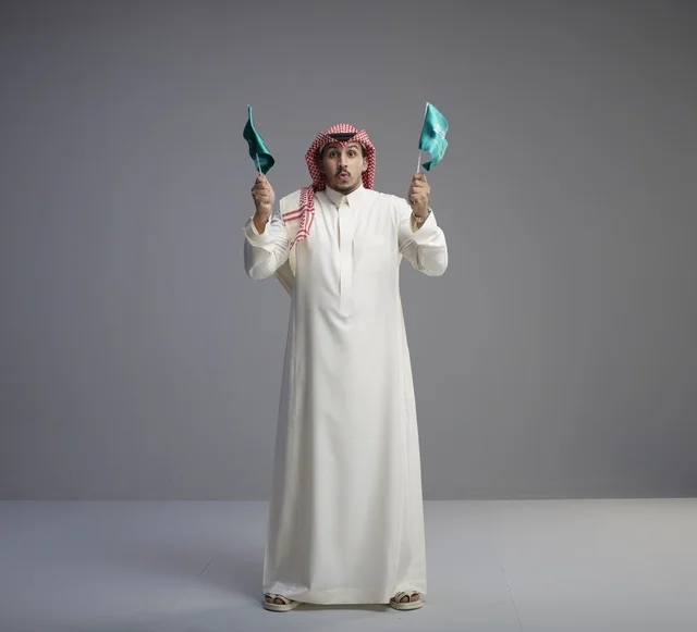رجل سعودي بالزي التقليدي يحمل العلم السعودي في الاستوديو