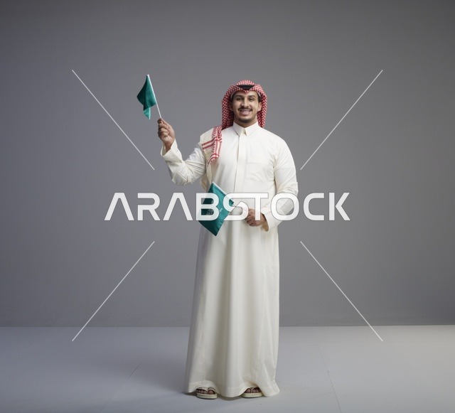رجل سعودي يرتدي الثوب التقليدي ويحمل علم السعودية