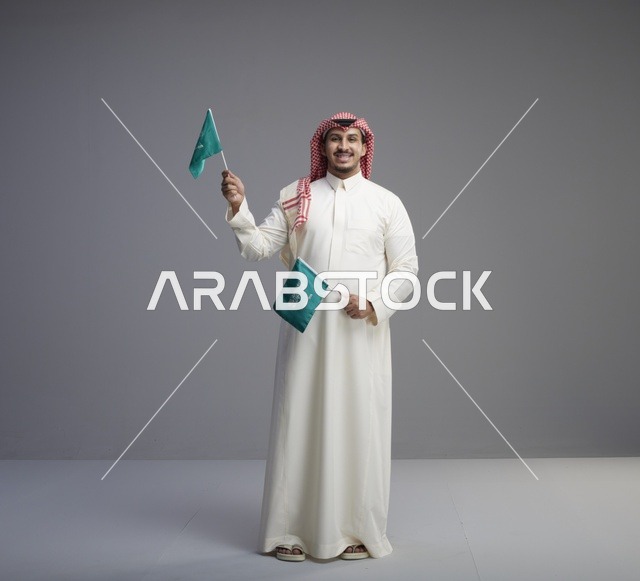 رجل سعودي يحمل العلم السعودي بالثوب التقليدي