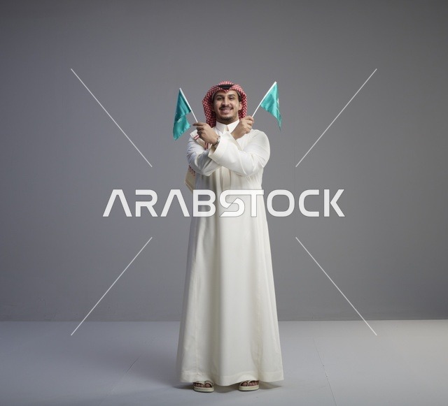 رجل سعودي يحمل الأعلام السعودية بخلفية استوديو