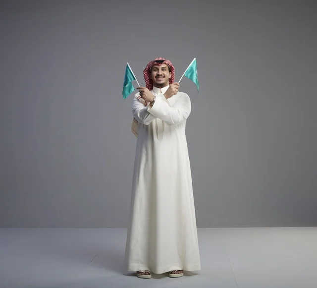 رجل سعودي يحمل الأعلام السعودية بخلفية استوديو