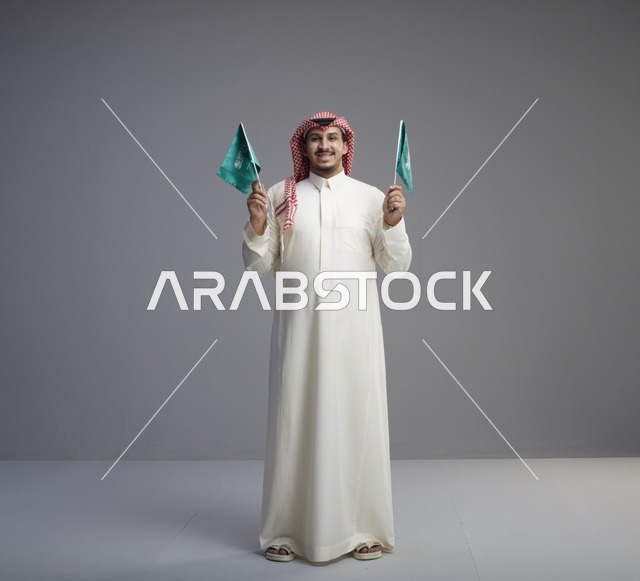 رجل سعودي يحمل علمين سعوديين في الاستوديو