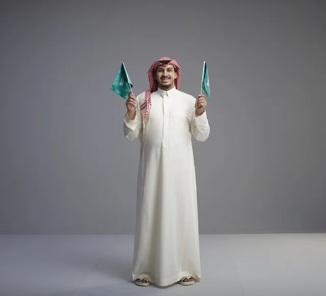 رجل سعودي يحمل علمين سعوديين في الاستوديو