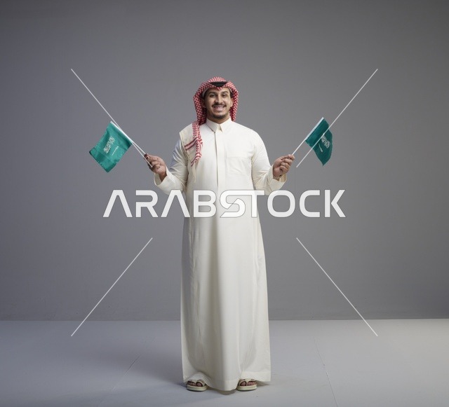 رجل سعودي يحمل علمين سعوديين في الاستوديو