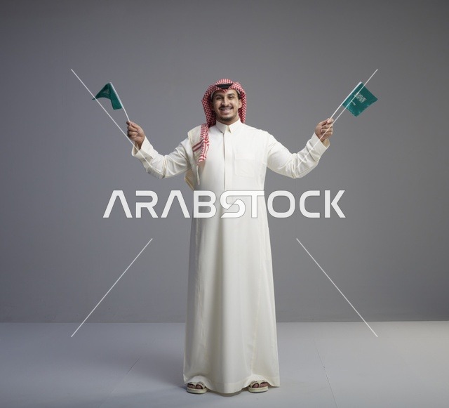 رجل سعودي مبتسم يحمل أعلام السعودية في تصوير استوديو