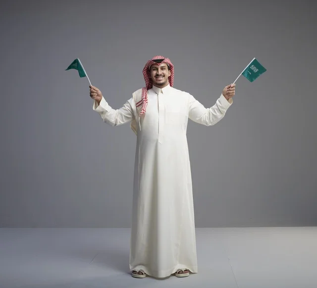 رجل سعودي مبتسم يحمل أعلام السعودية في تصوير استوديو