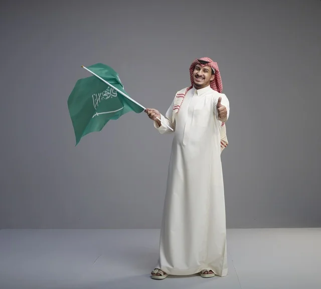 رجل سعودي يحمل العلم السعودي مع علامة الإبهام
