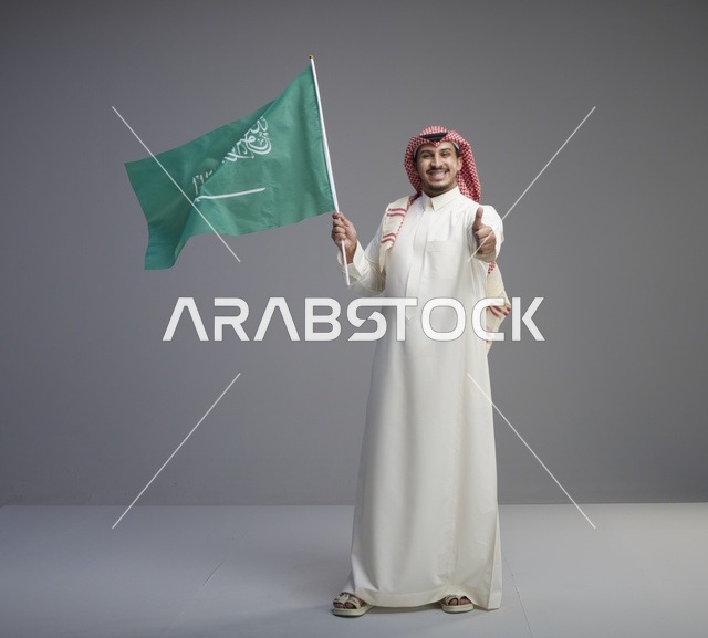 رجل سعودي يحمل علم السعودية مع إشارة الإعجاب