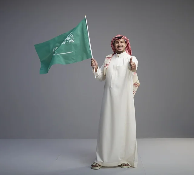 رجل سعودي يحمل علم السعودية مع إشارة الإعجاب