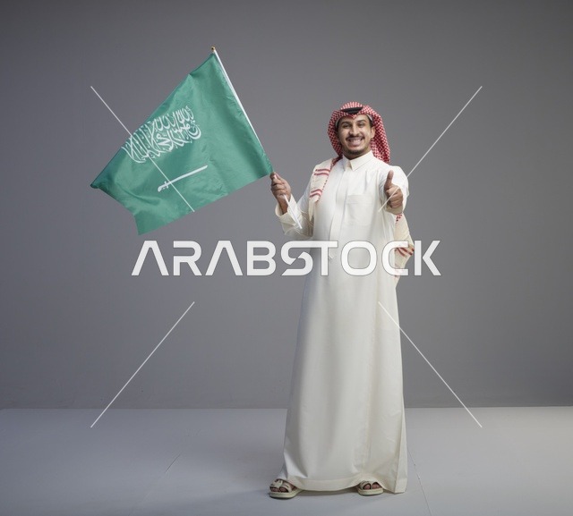 رجل سعودي يلوح بالعلم الوطني مع إشارة الإبهام