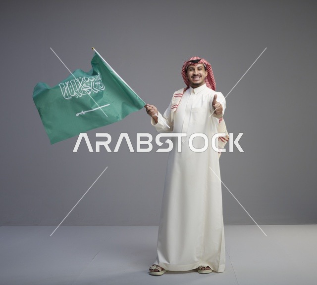 رجل سعودي يحمل العلم السعودي ويشير بالإبهام