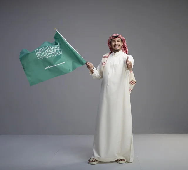 رجل سعودي يحمل العلم السعودي ويشير بالإبهام