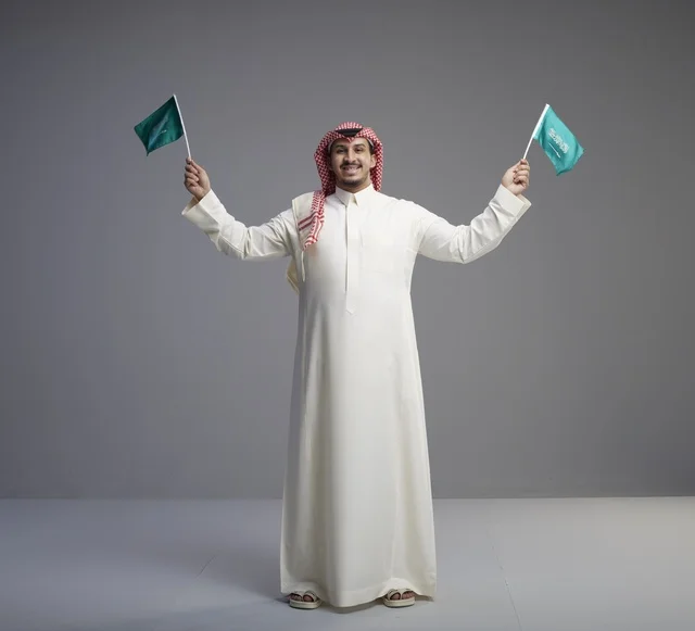 Saudi Man Holding National Flags Against Gray Background - Photo