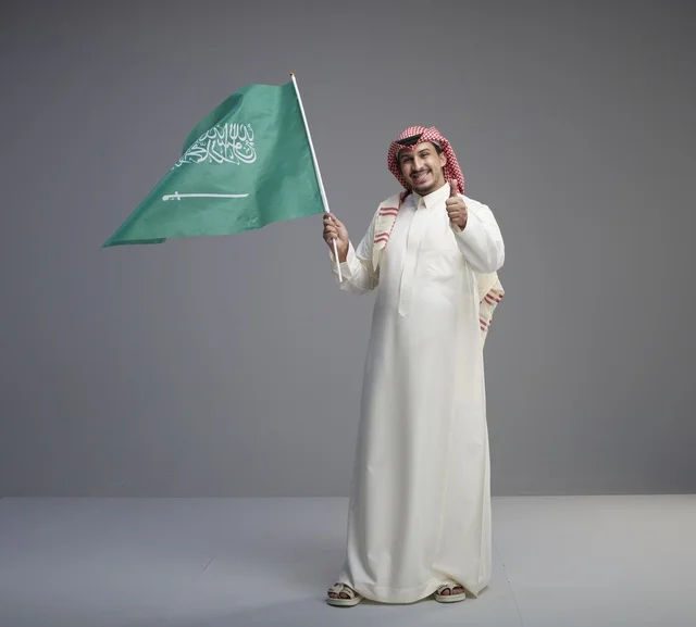 رجل سعودي يحمل علم السعودية مع إشارة الإبهام والرضا
