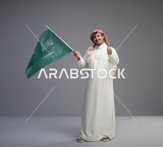 رجل سعودي يرفع العلم الوطني ويشير بعلامة الإعجاب