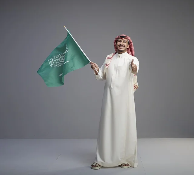 رجل سعودي يحمل العلم الوطني مع إشارة الإعجاب بيده