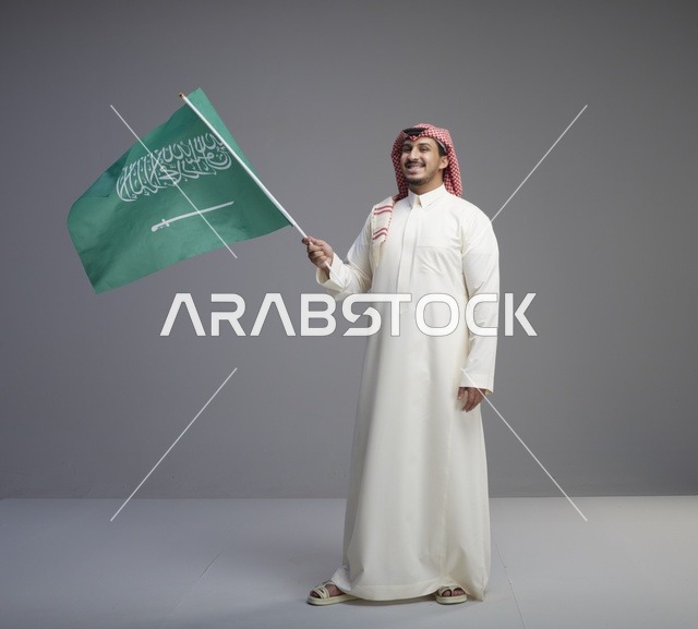 رجل سعودي يلوح بالعلم بالزي التقليدي في استوديو
