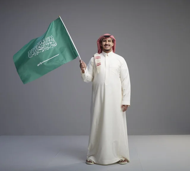 رجل سعودي بالزي التقليدي يحمل علم السعودية
