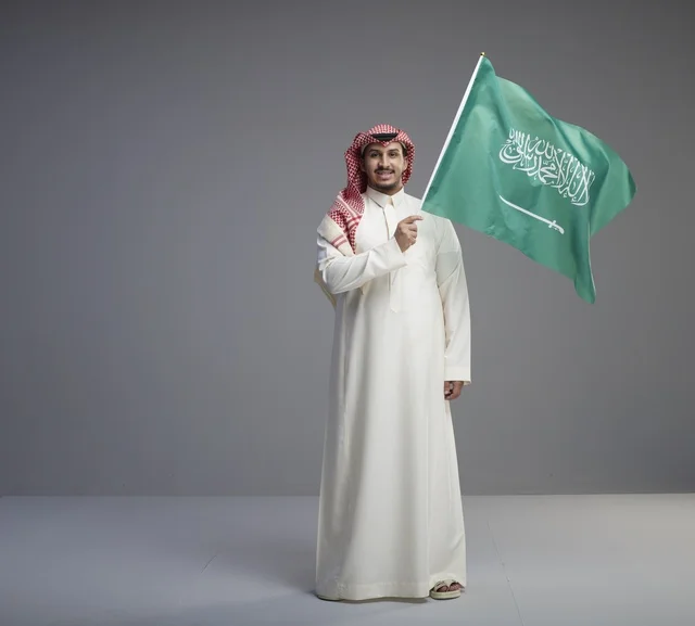 رجل سعودي يرفع العلم الوطني في استوديو بخلفية رمادية