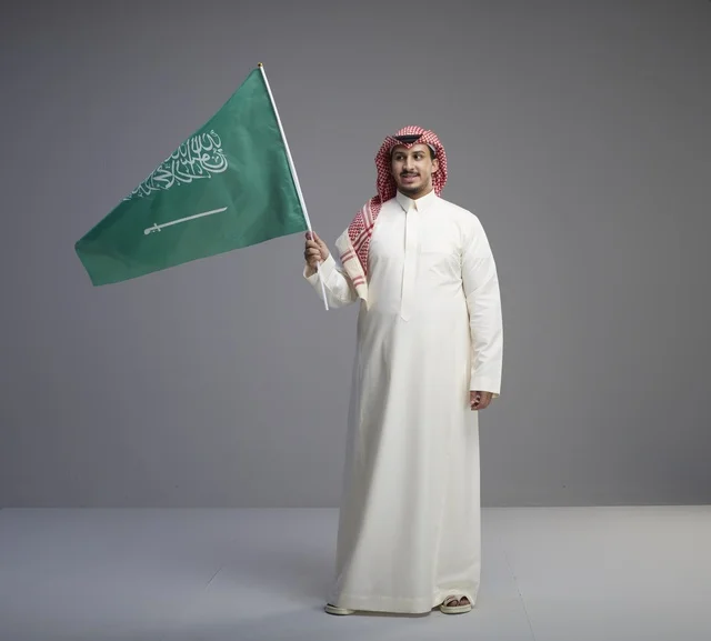 رجل سعودي يمسك العلم الوطني بالزي التقليدي