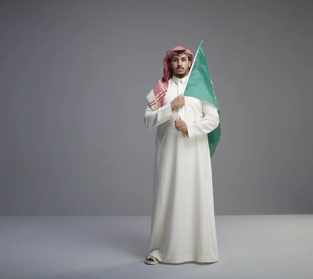 رجل سعودي بالزي التقليدي يمسك علم المملكة العربية السعودية