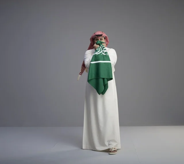 رجل سعودي بالزي التقليدي يحمل العلم السعودي