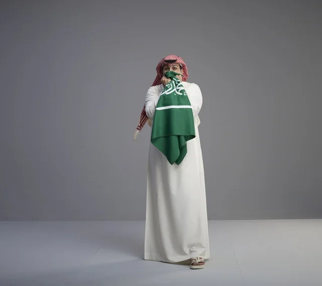 رجل سعودي يقبل العلم السعودي خلفية رمادية
