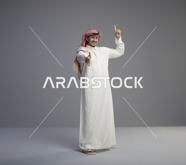 رجل سعودي بالزي التقليدي يشير للأعلى بابتسامة واثقة